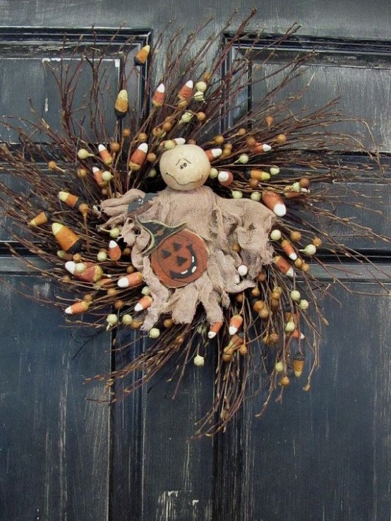 a rustic Halloween wreath of branches, candy corns, a burlap ghost and a pumpkin of wood