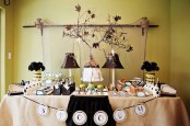 a dessert table with a burlap tablecloth, rustic vintage table lamp, dried leaves and blooms and dark blooms