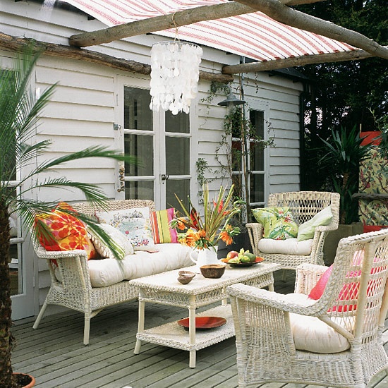 a neutral meets rustic patio with white wicker furniture, bright textiles and a shell chandelier