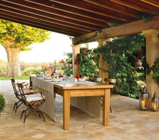 a cozy rustic patio with a dining space -a wooden table and some refined chairs plus blooms and candle lanterns