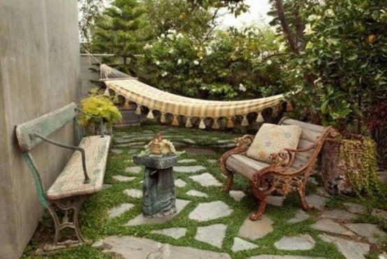 a backyard patio with some vintage furniture, a hammock, some pots and a stone floor with grass