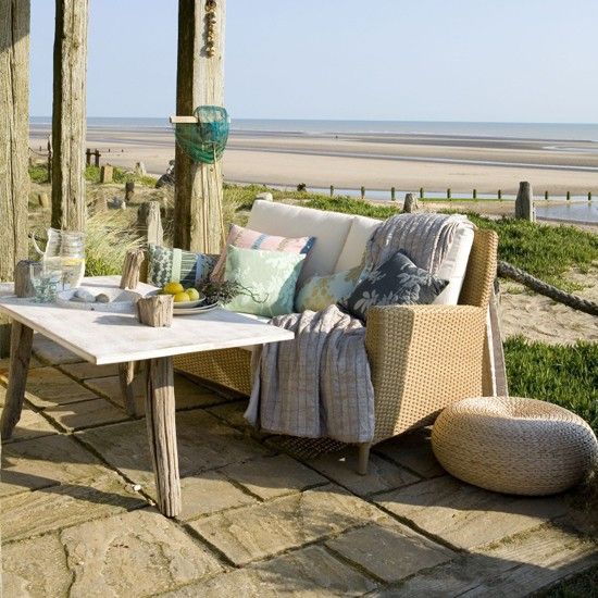 a neutral rustic patio with wicker and wooden furniture, bright printed textiles and a little ottoman