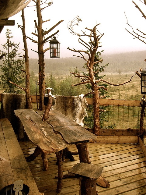 a rustic mountain patio with rough wooden furniture, stools, logs and candle lanterns