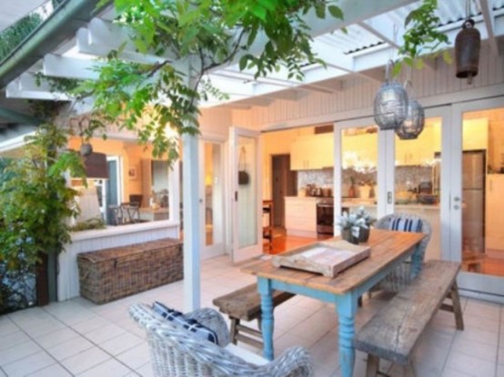 a neutral rustic patio with a wooden dining set and wicker lamps over it plus wicker chests