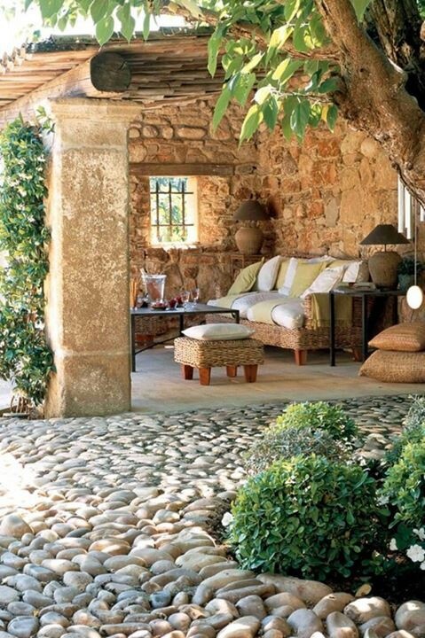 a rustic patio done with stone walls, wicker furniture, neutral textiles and lamps