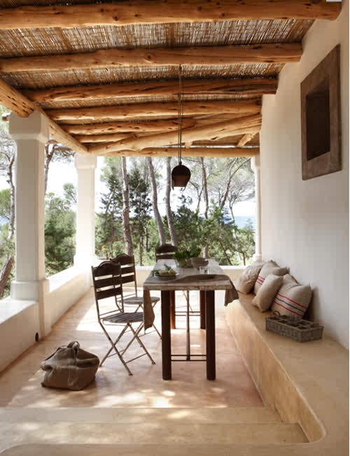 a neutral rustic patio with wooden furniture, a concrete bench going along the patio and pendant lanterns