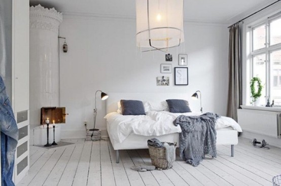 an airy Scandinavian bedroom with a white stove, an upholstered bed, a pendant lamp, storage units and lamps
