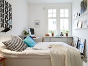 a small Scandinavian bedroom with a white bed, open shelves for storage, a desk in the corner and some graphics