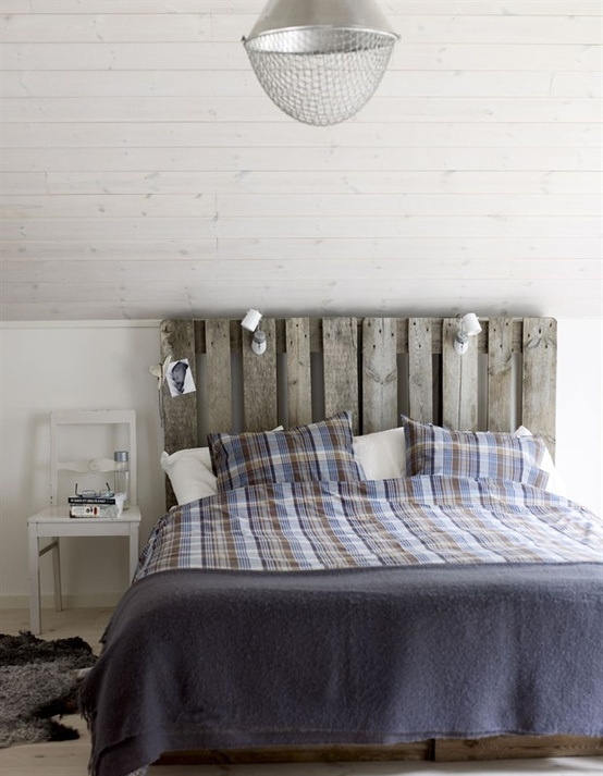 a rustic Nordic bedroom with a shiplap ceiling, a weathered wood bed, a white chair and a pendant lamp