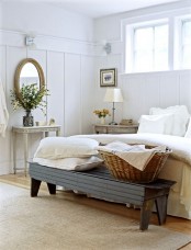 a rustic meets Nordic bedroom with a dark bench, vintage furniture, a mirror, a whitewashed nightstand and a lamp