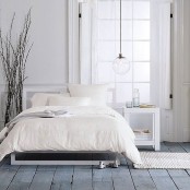 a simple Nordic bedroom with a whitewashed wooden floor, a pendant lamp, modern white furniture and a branch arrangement