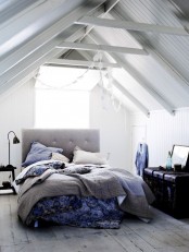 a light-filled Nordic bedroom with white planks and beams on the ceiling, a grey uphosltred bed and bright bedding