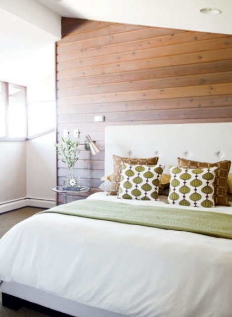 a welcoming bedroom decorated with a stained wooden wall, an upholstered white bed and printed pillows