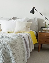 a Nordic bedroom with neutral bedding, a wooden nightstand, a black lamp