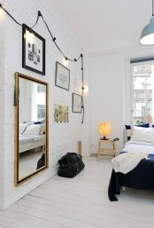 a Nordic bedroom with white brick walls, a gallery wall with mirrors and artworks, a bed and step stools as nightstands