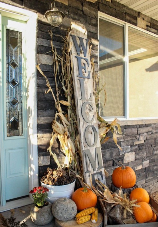natural orange pumpkins, pinecones, corn, wheat, corn husks and a large Welcome sign for a rustic Thanksgiving porch