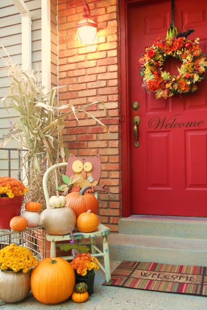 bright fall pumpkins, bright fall blooms in pots, corn husks and a wreath of bold fall leaves on the door