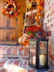 a candle lantern, faux pumpkins and leaves, a lush wreath of fall leaves, pumpkins and pinecones for Thanksgiving