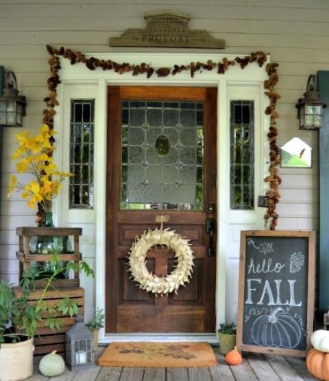 a pinecone garland, a fall leaf arrangement, a fall sign, natural pumpkins and candle lanterns for a Thanksgiving front door and porch