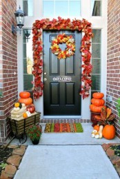 a bright fall leaf garland and wreath, stacks of pumpkins, hay, gourds and greenery for a chic front door