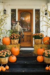 hay, bold orange pumpkins and bold orange blooms in baskets, corn husks and a scarecrow make the front door and porch bold and bright