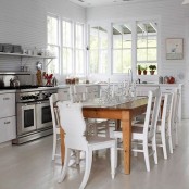 a modern white kitchen with white cabinets and walls, with a whitewashed floor, white chairs and a stained dining table