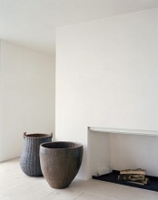 a minimalist living room with a fireplace, white walls and a whitewashed floor plus contrasting vases and pots