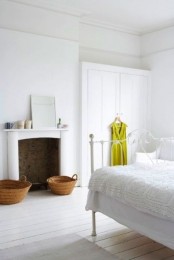 a white vintage bedroom with white walls and whitewashed floors, a non-working fireplace and white furniture