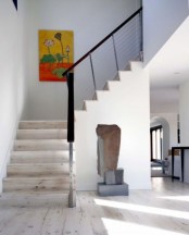 a chic foyer with a bright artwork, white walls and a whitewashed floor and matching stairs