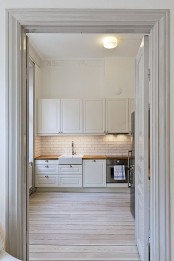 an off-white kitchen with a subway tile backsplash and a whitewashed wooden floor plus off-white doors