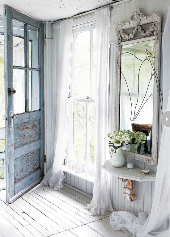 a shabby chic entryway with white walls, a whitewashed floor, a blue door and vintage furniture