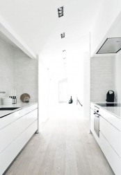 a white minimalist kitchen with a whitewashed floor, sleek cabinets and a white tile backsplash