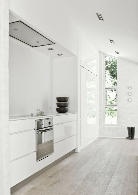 a white minimalist kitchen with whitewashed wooden floor that brings a bit of a natural touch and warmth to the space