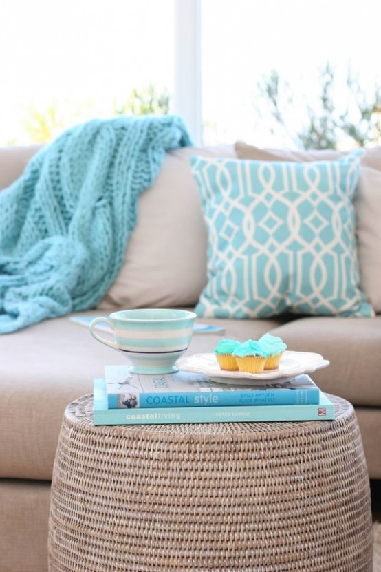 a dove grey sofa with blue printed pillows, a white wicker coffee table with blue books are great for a coastal space