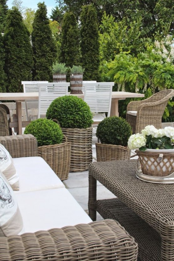 an outdoor space with timeless elegance. with wicker chairs, a sofa and stools, with a wicker table, white upholstery and lots of potted greenery
