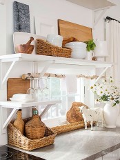 a rustic white kitchen with open shelves, white porcelain and wicker baskets for storage, a branch for hanging towels is cozy