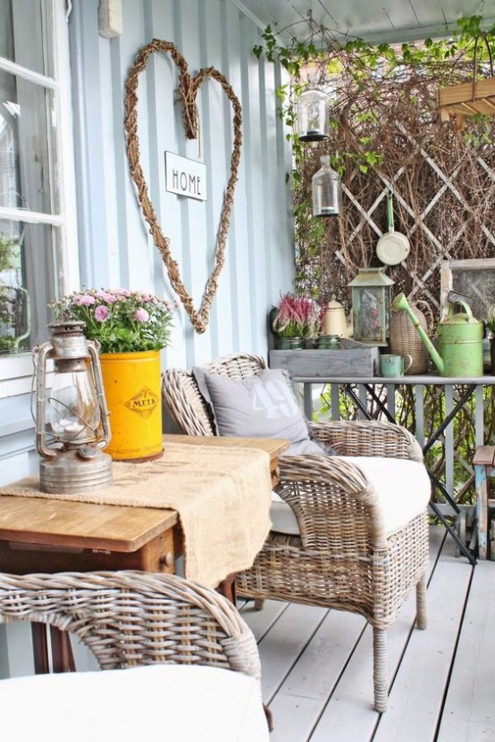 a farmhouse porch with a wooden table and wicker chairs, vintage lanterns and blooms, baskets for storage