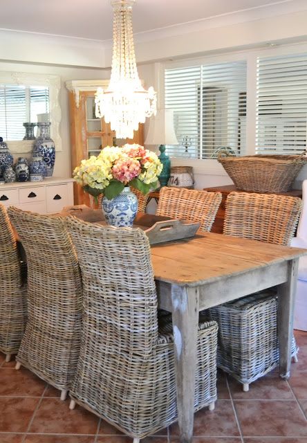 a farmhouse dining space with a wooden table, wicker chairs, blooms in a vase and a statement crystal chandelier