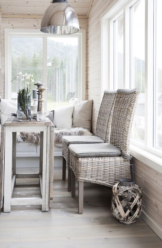 a neutral Scandinavian sunroom with a built-in seat with faux fur and neutral pillows, a shabby chic table and neutral wicker chairs, candles and candle lanterns