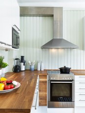 rich stained butcherblock countertops bring a rustic feel to this farmhouse kitchen and make it look cozier and warmer