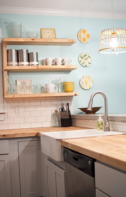 a dove grey kitchen with light stained wooden countertops and wall mounted shelves that match