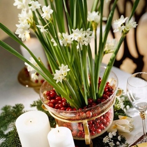 a catchy Christmas centerpiece with moss, pillar candles, a pot wih cranberries and blooms is a chic idea