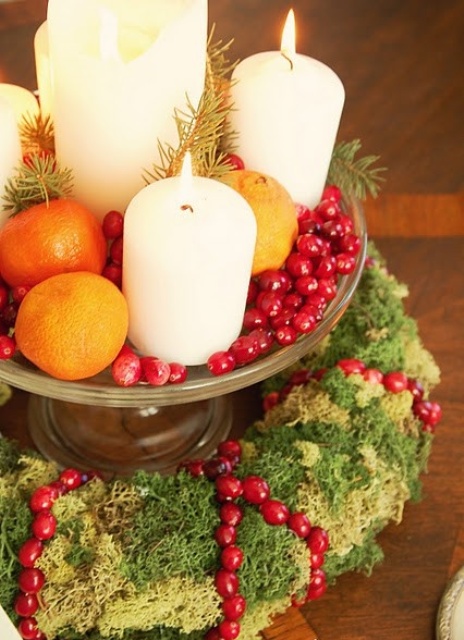 a natural Christmas centerpiece of a moss wreath, a vintage bowl with citrus and cranberries, pillar candles and cranberries over the moss