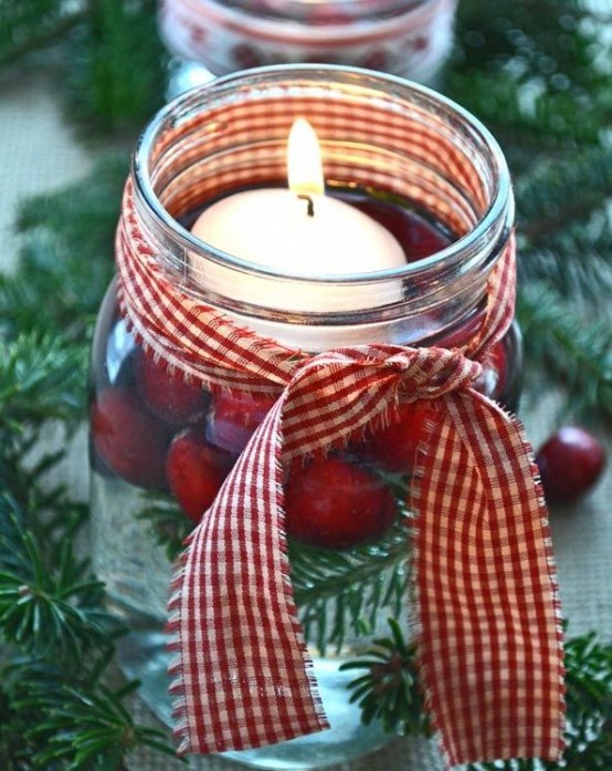 a glass jar with evergreens, cranberries, a floating candle and a red plaid ribbon is a lovely decoration for Christmas