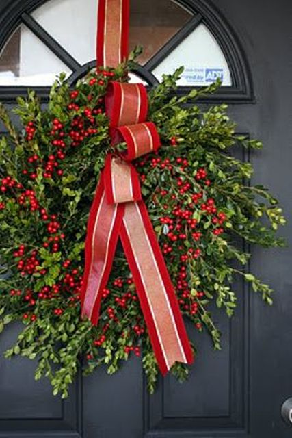 a greenery wreath with cranberries and red striped ribbon bow in the center is a bold and cool decoration for a front door