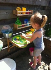 a colorful outdoor kitchen with wooden shelves, colorful plastic tableware and toys for having fun
