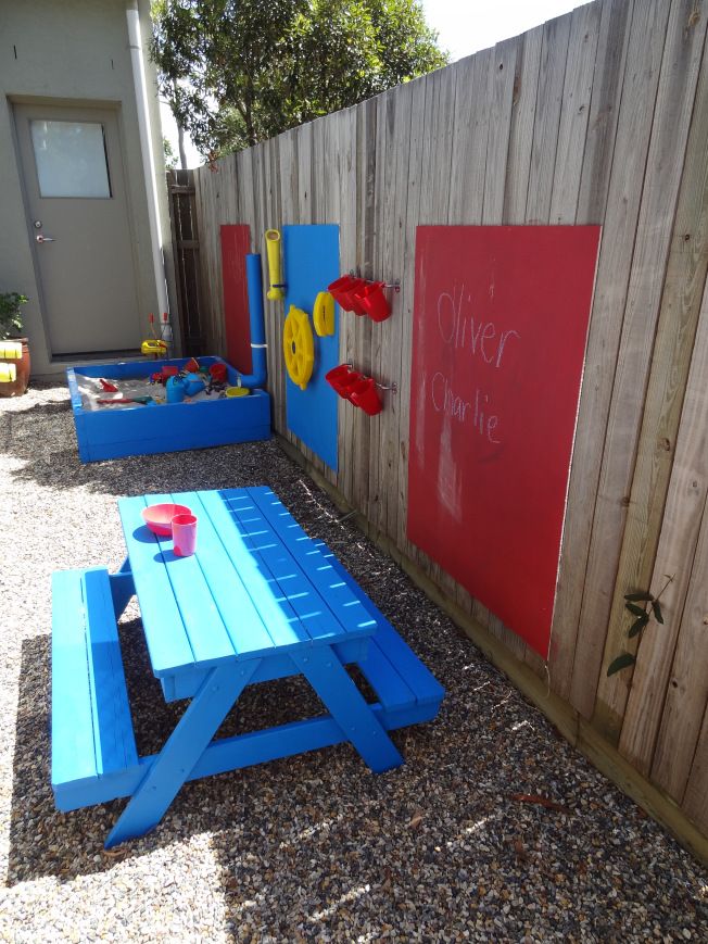 a colorful outdoor space with a blue dining set, colorful chalkboards and a blue sand box with various stuff for playing