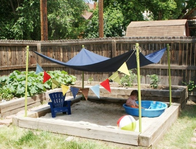 a simple outdoor sand box with a canopy, colorful buntings, balls and a plastic bathtub is a perfect idea for your garden