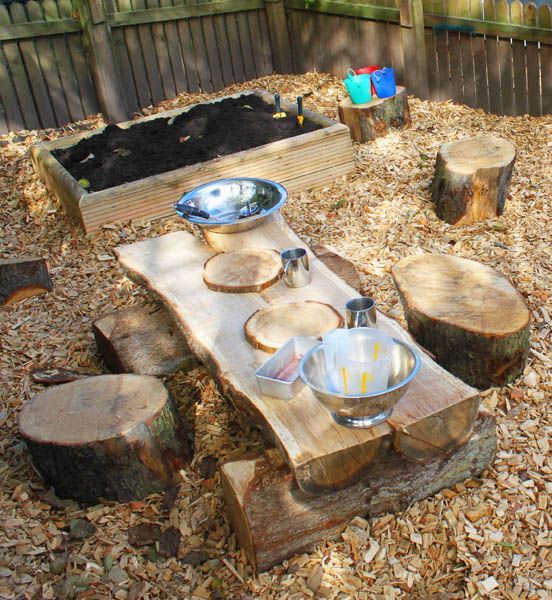 a simple rustic place space with a sand box, a wooden table and tree stump stools plus some metal tableware to play with