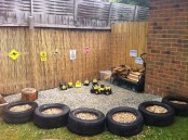 a simple playground with lots of toy cars, signs, wood is lined up with old tyres filled with sand